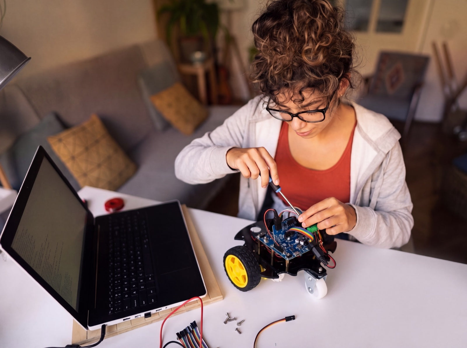 Een tiener schroeft aan de SyncGear 2WD robot, met een laptop en losse kabeltjes op tafel