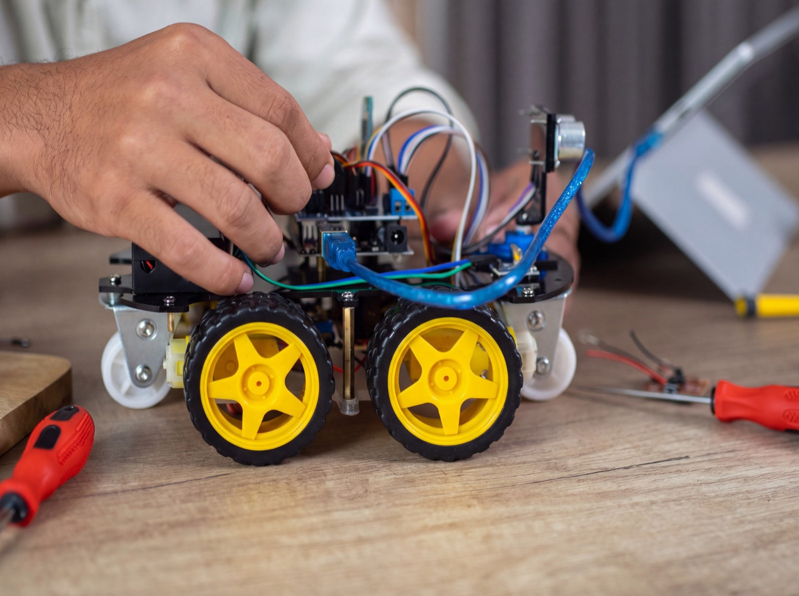 Handen sluiten de bedrading aan op de SyncGear robot, met schroevendraaiers op tafel